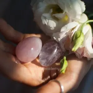 twee vrouwenhanden met twee yoni eieren daarin. Witte bloemen aan de zijkant